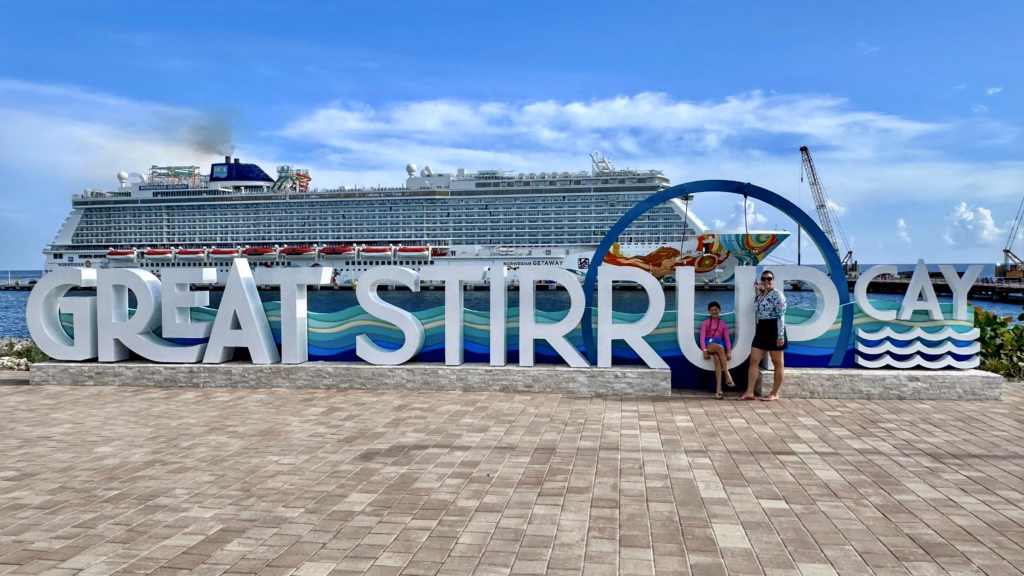 Adventure-Seeking Mom Alisha dos Santos and daughter pose with Great Stirrup Cay sign and Norwegian Getaway cruise ship in The Bahamas